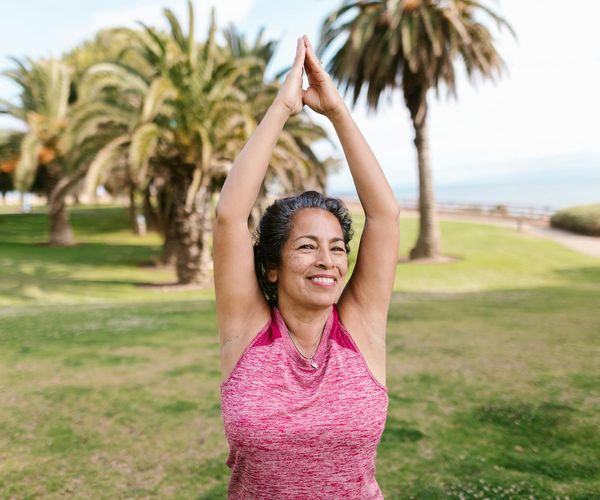 Smiling woman stretching outdoors during a sunny morning.